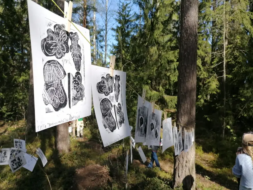 Paperille tehtyjä mustavalkoisia taideteoksia metsässä, puiden väliin ripustettuna.