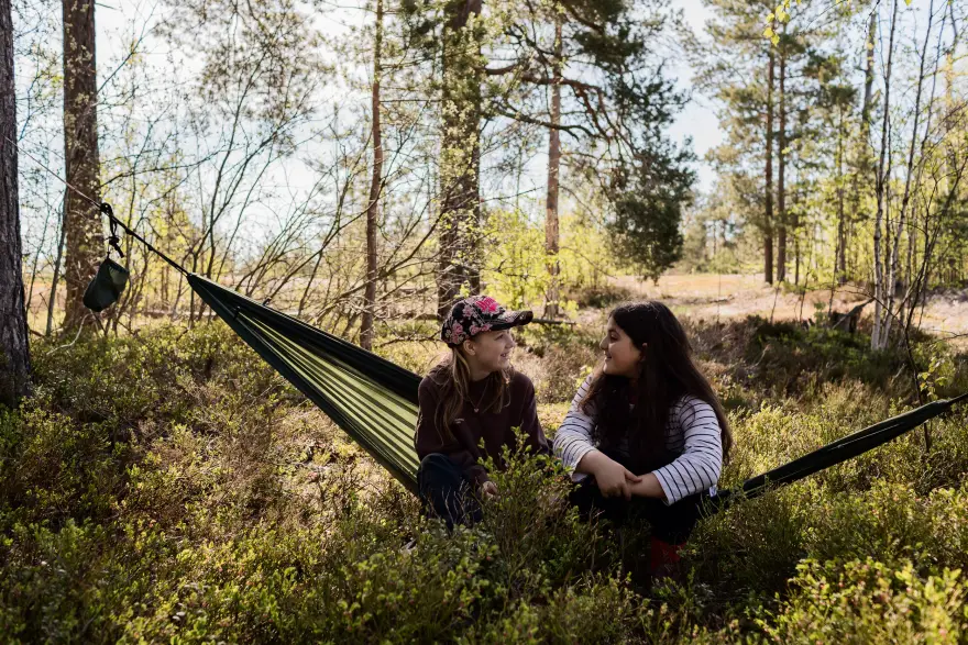 Kaksi tyttöä istuvat riippumatolla syskyisessä metsässä Kulttuurikeskus Stoan retkellä.