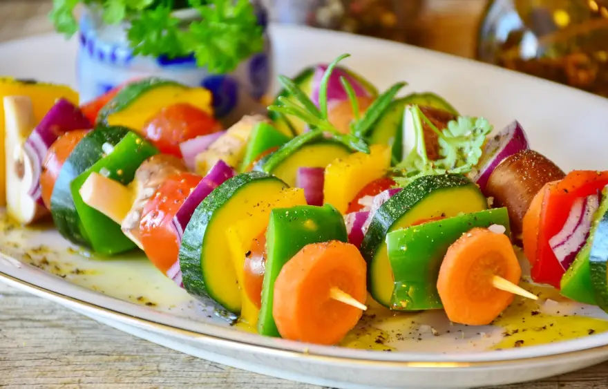 The image shows colorful vegetable skewers with carrot, bell pepper, tomato, zucchini, and red onion.