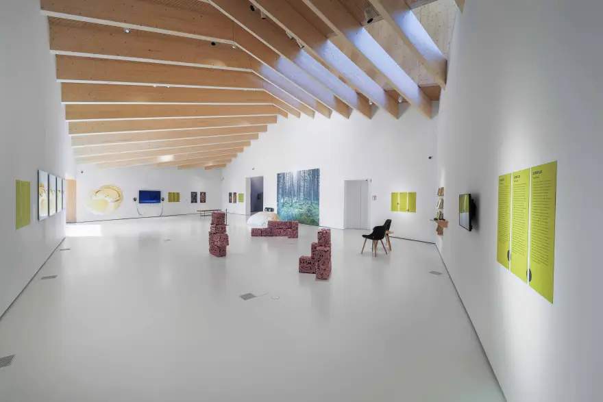 View of the Chappe art space exhibition hall. Many works made of different materials are on display. The exhibition hall is white with wooden elements on the ceiling.