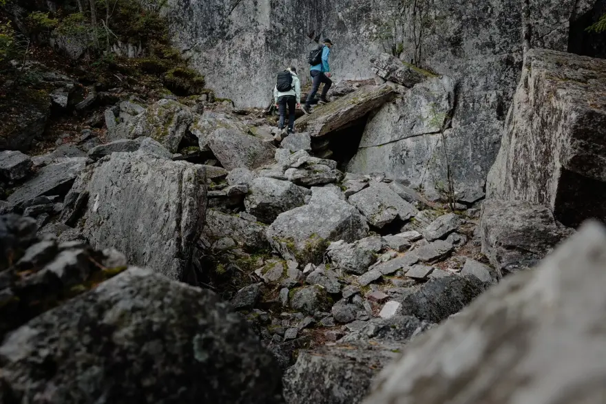 Two people in hiking clothes are walking uphill on a rocky mountainside.